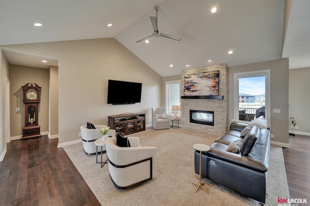 living area with wood finished floors, a ceiling fan, a fireplace, vaulted ceiling, and a wealth of natural light