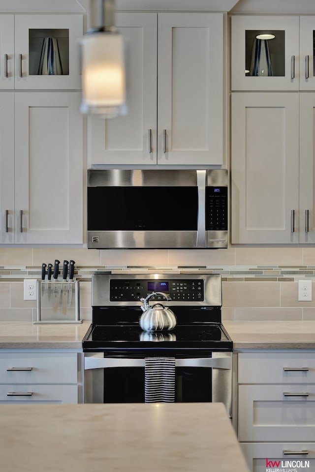 kitchen featuring stainless steel appliances, glass insert cabinets, backsplash, and white cabinets