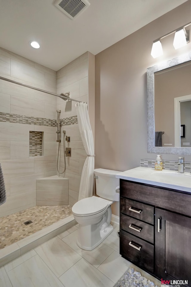 bathroom featuring visible vents, baseboards, toilet, tiled shower, and vanity