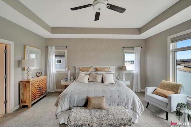 carpeted bedroom with a raised ceiling, a ceiling fan, and baseboards