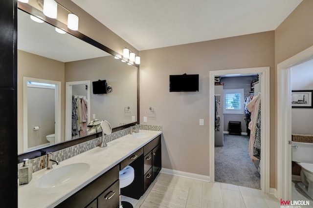 bathroom with a sink, baseboards, toilet, and double vanity