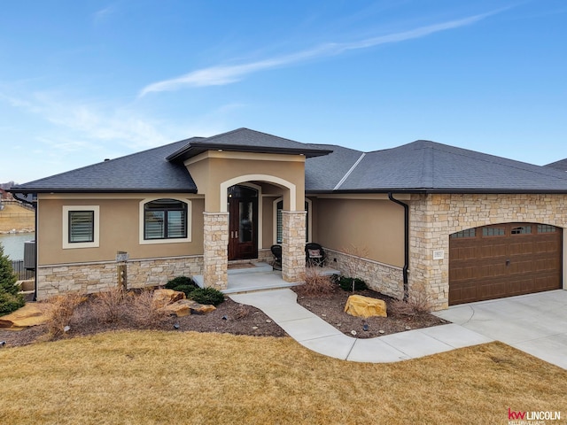 prairie-style house featuring a shingled roof, stucco siding, a garage, stone siding, and driveway