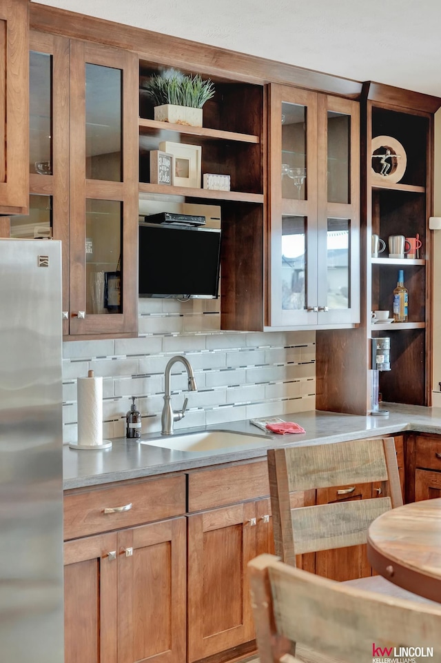 kitchen featuring backsplash, open shelves, freestanding refrigerator, and a sink