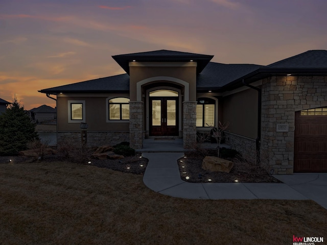 exterior entry at dusk featuring french doors, stone siding, a garage, and stucco siding