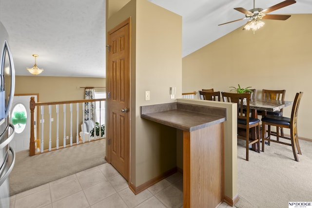 kitchen featuring light tile patterned floors, lofted ceiling, light colored carpet, and dark countertops