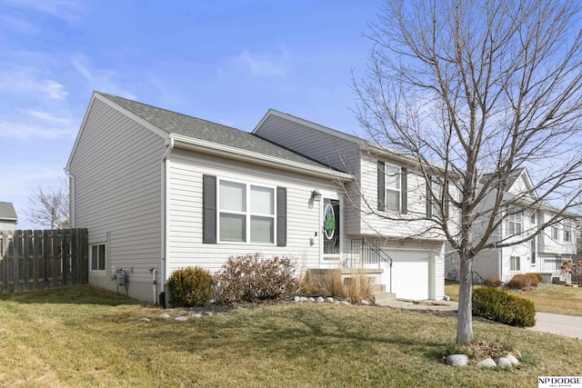 tri-level home with an attached garage, a shingled roof, a front yard, and fence