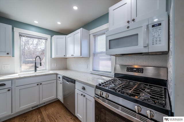 kitchen featuring dark wood-type flooring, a sink, stainless steel appliances, white cabinets, and light stone countertops