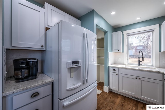 kitchen featuring light stone counters, dark wood-style floors, visible vents, a sink, and white fridge with ice dispenser