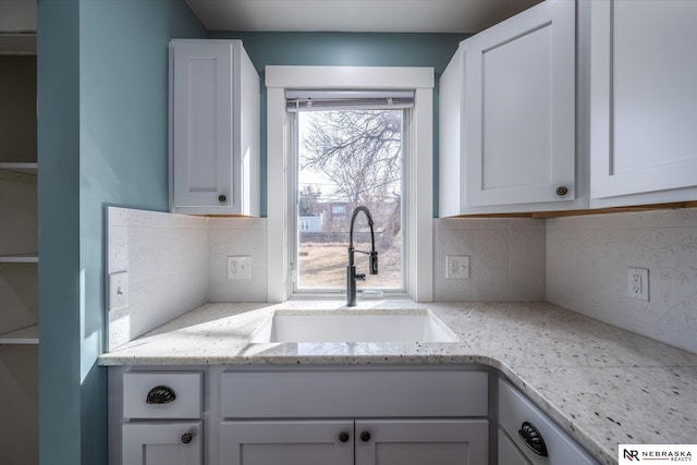 kitchen featuring decorative backsplash, light stone countertops, white cabinetry, and a sink