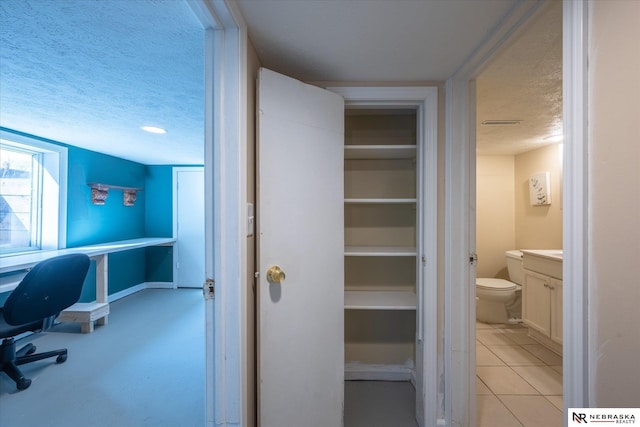 interior space with vanity, baseboards, tile patterned flooring, a textured ceiling, and toilet