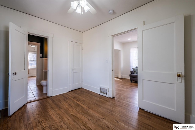 unfurnished bedroom with dark wood finished floors, visible vents, connected bathroom, and baseboards