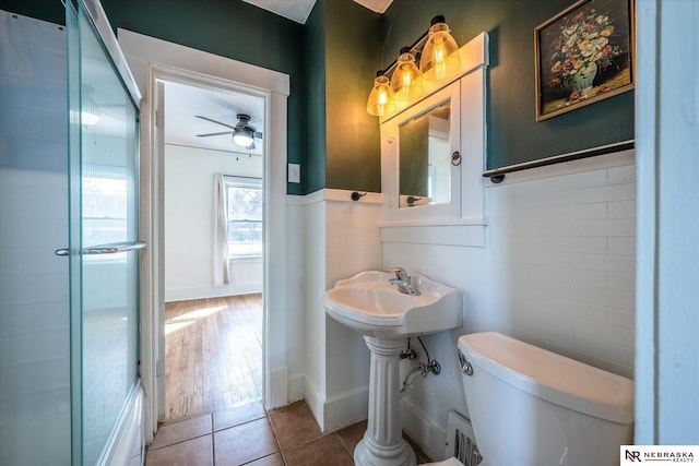 bathroom with a wainscoted wall, toilet, tile walls, tile patterned flooring, and ceiling fan