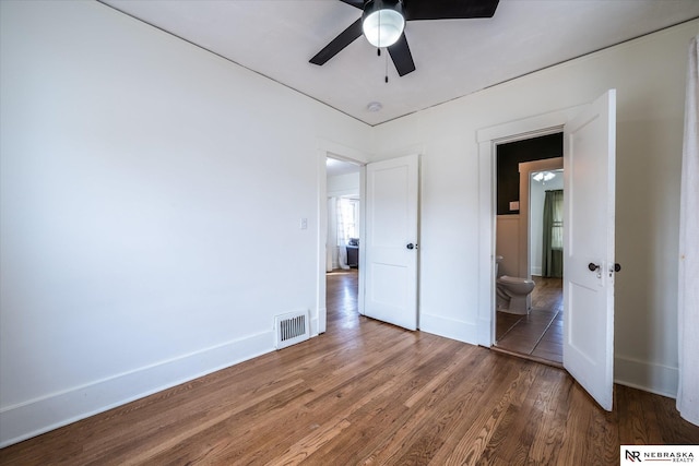 unfurnished bedroom with wood finished floors, visible vents, ensuite bathroom, and baseboards