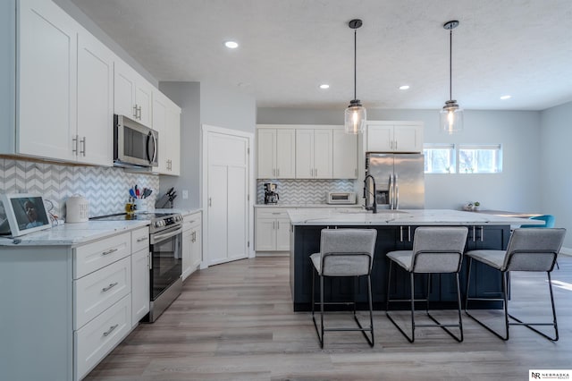 kitchen featuring a kitchen bar, white cabinets, light wood-style floors, and stainless steel appliances