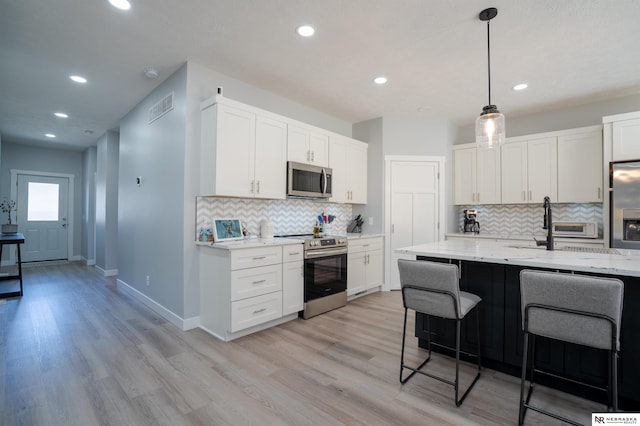 kitchen featuring a kitchen bar, visible vents, light wood-style flooring, light stone counters, and stainless steel appliances