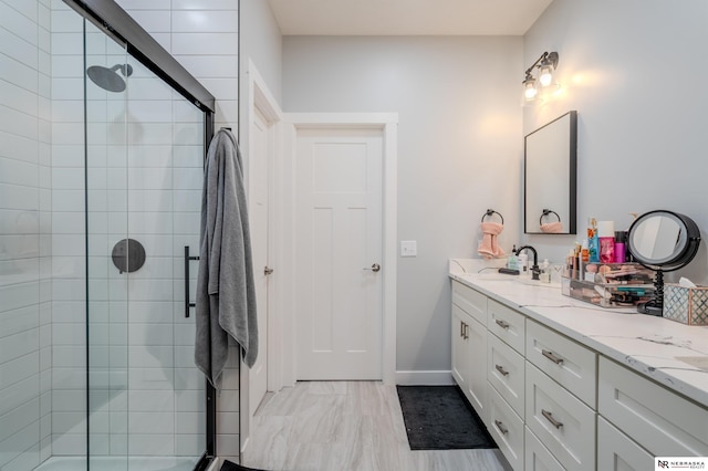 full bathroom featuring double vanity, a shower stall, baseboards, and a sink