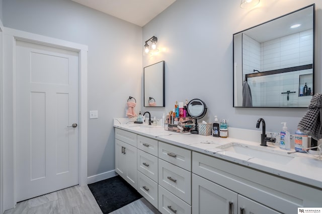 full bath featuring double vanity, tiled shower, baseboards, and a sink