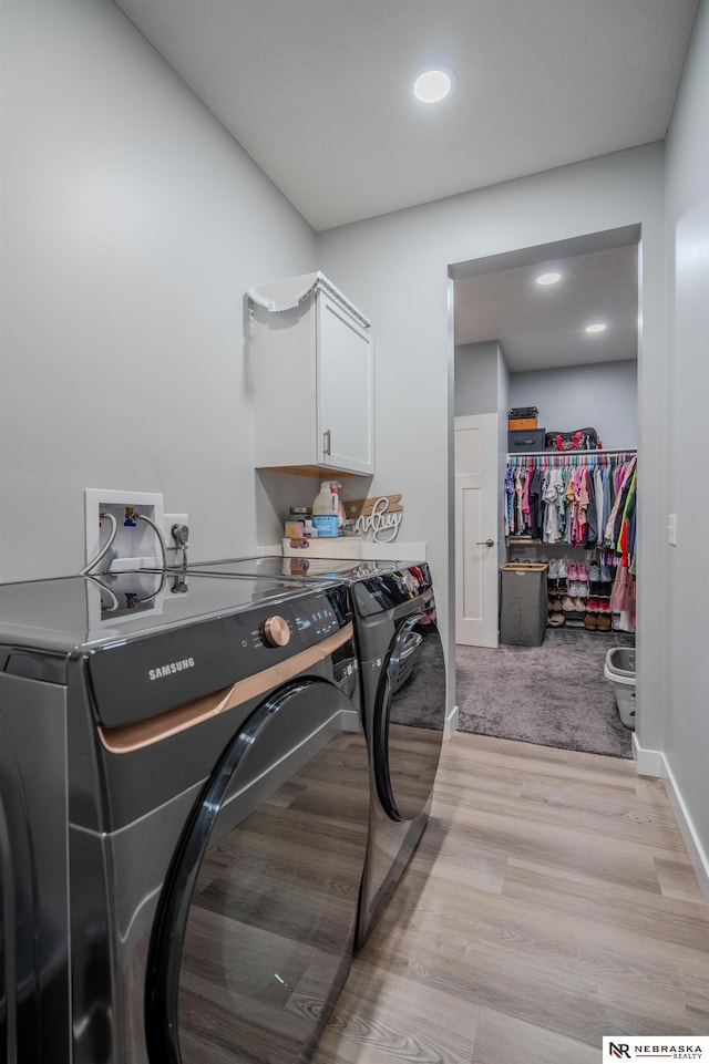 clothes washing area with cabinet space, light wood-style flooring, baseboards, and separate washer and dryer