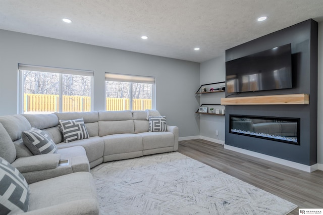 living room with a glass covered fireplace, a textured ceiling, baseboards, and wood finished floors