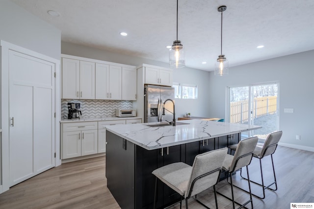 kitchen featuring tasteful backsplash, light wood-style flooring, white cabinets, stainless steel fridge, and a kitchen island with sink