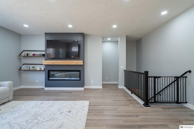 living room with recessed lighting, baseboards, wood finished floors, and a glass covered fireplace