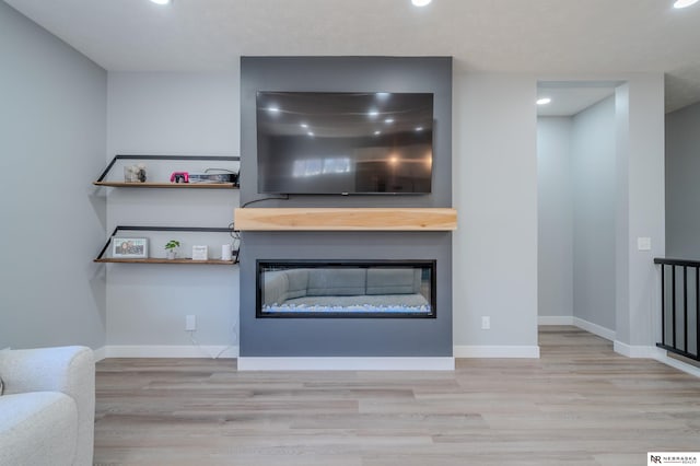 unfurnished living room with baseboards, wood finished floors, and a glass covered fireplace