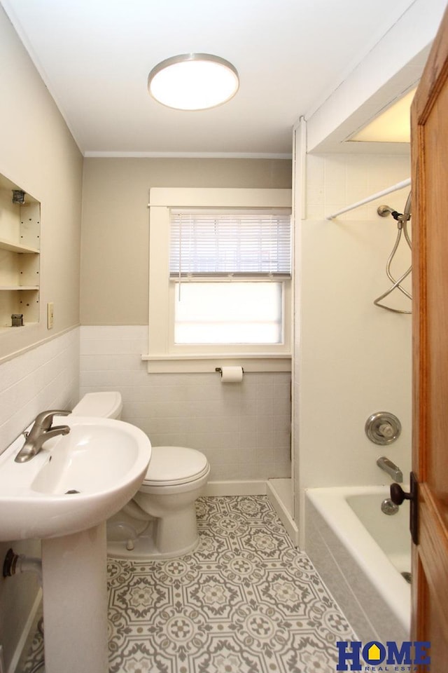 bathroom with toilet, wainscoting, tile patterned floors, tile walls, and  shower combination