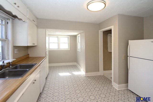 kitchen with a sink, white appliances, white cabinets, light countertops, and baseboards