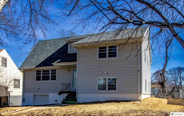 back of house featuring a garage, roof with shingles, and fence