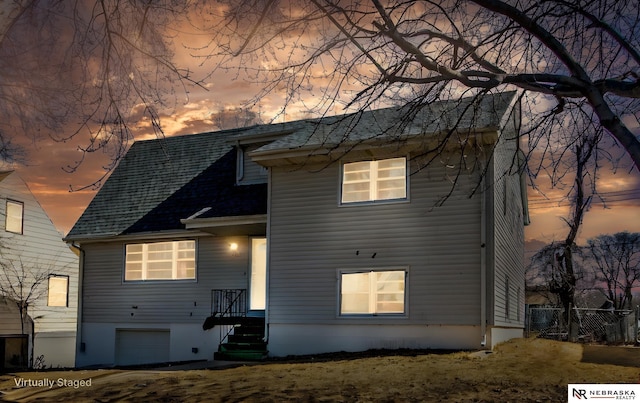 rear view of property featuring an attached garage, a shingled roof, and fence