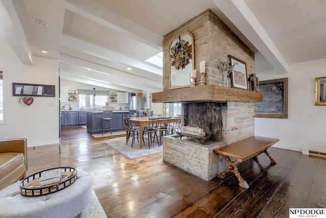 living room with lofted ceiling with beams, baseboards, a stone fireplace, and hardwood / wood-style flooring