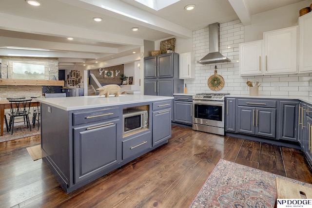 kitchen with beamed ceiling, gray cabinetry, white cabinetry, appliances with stainless steel finishes, and wall chimney range hood