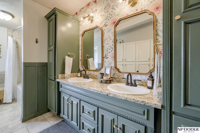 bathroom with a sink, double vanity, wainscoting, and wallpapered walls