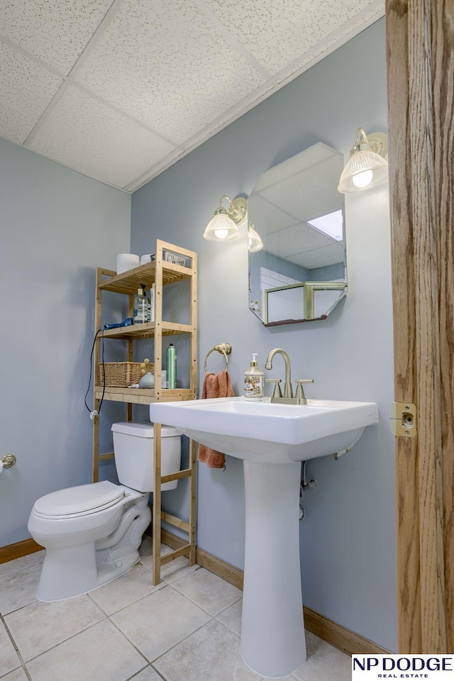 bathroom featuring tile patterned flooring, baseboards, a drop ceiling, toilet, and a sink