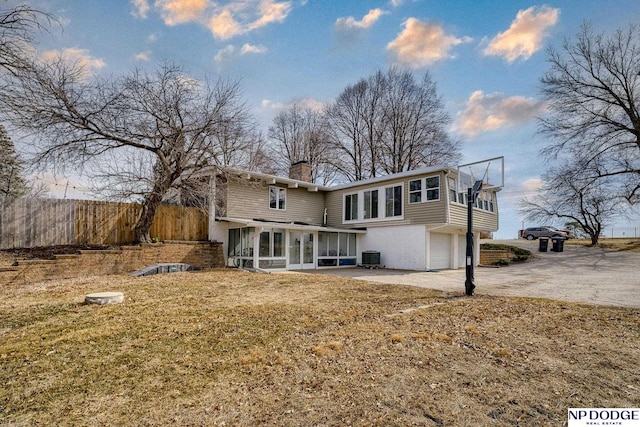 rear view of house with fence, concrete driveway, a chimney, a garage, and a sunroom