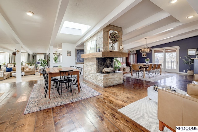 dining space featuring a stone fireplace, vaulted ceiling with skylight, baseboards, and wood-type flooring