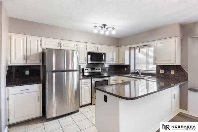 kitchen with a peninsula, a sink, decorative backsplash, stainless steel appliances, and white cabinetry