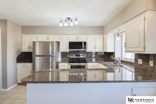 kitchen featuring a sink, a textured ceiling, stainless steel appliances, a peninsula, and decorative backsplash