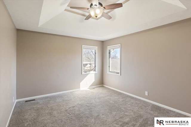 carpeted spare room featuring baseboards, a raised ceiling, and ceiling fan