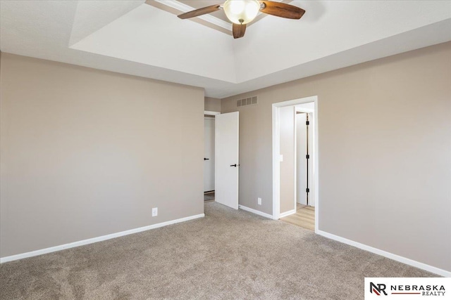 unfurnished bedroom featuring visible vents, baseboards, ceiling fan, light colored carpet, and a tray ceiling