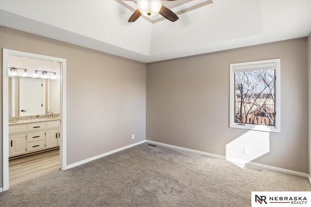 unfurnished bedroom with ensuite bath, a tray ceiling, baseboards, and light carpet