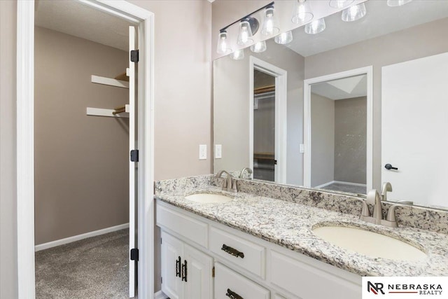 bathroom featuring double vanity, a spacious closet, baseboards, and a sink