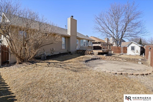 rear view of property with an outbuilding, fence, a wooden deck, a chimney, and a storage unit