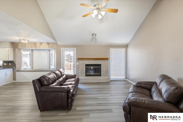 living area with light wood finished floors, a fireplace, high vaulted ceiling, and baseboards