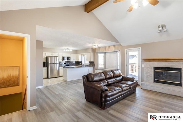 living room featuring beamed ceiling, high vaulted ceiling, light wood-style floors, a brick fireplace, and ceiling fan