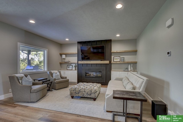 living room with a textured ceiling, wood finished floors, recessed lighting, a fireplace, and baseboards