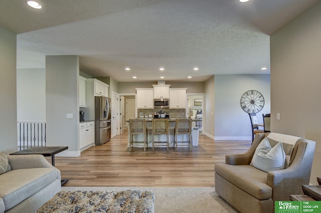 living room with a textured ceiling, recessed lighting, light wood-type flooring, and baseboards