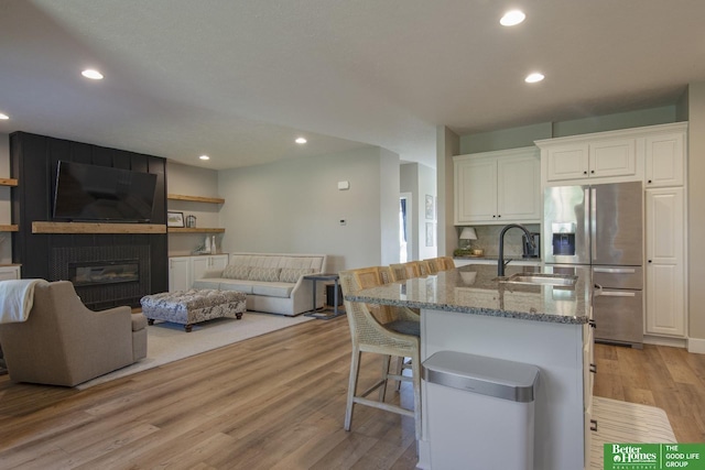 kitchen featuring light wood finished floors, stone counters, a fireplace, a sink, and stainless steel refrigerator with ice dispenser