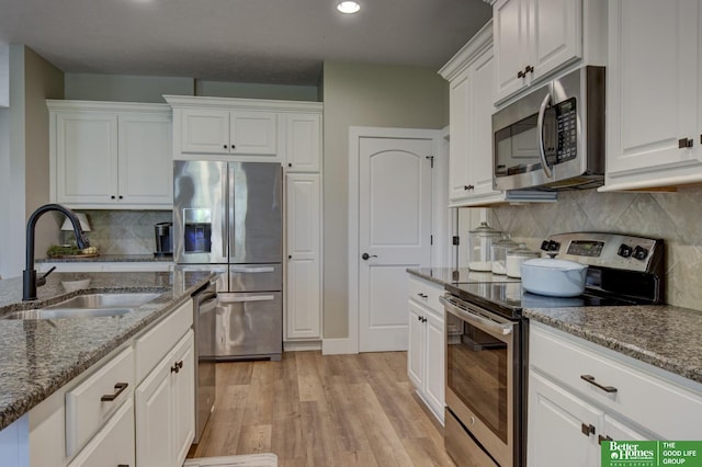 kitchen featuring a sink, stone countertops, white cabinetry, stainless steel appliances, and light wood finished floors