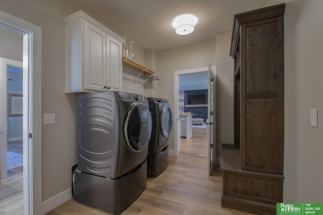 washroom with baseboards, light wood-type flooring, cabinet space, a textured ceiling, and independent washer and dryer